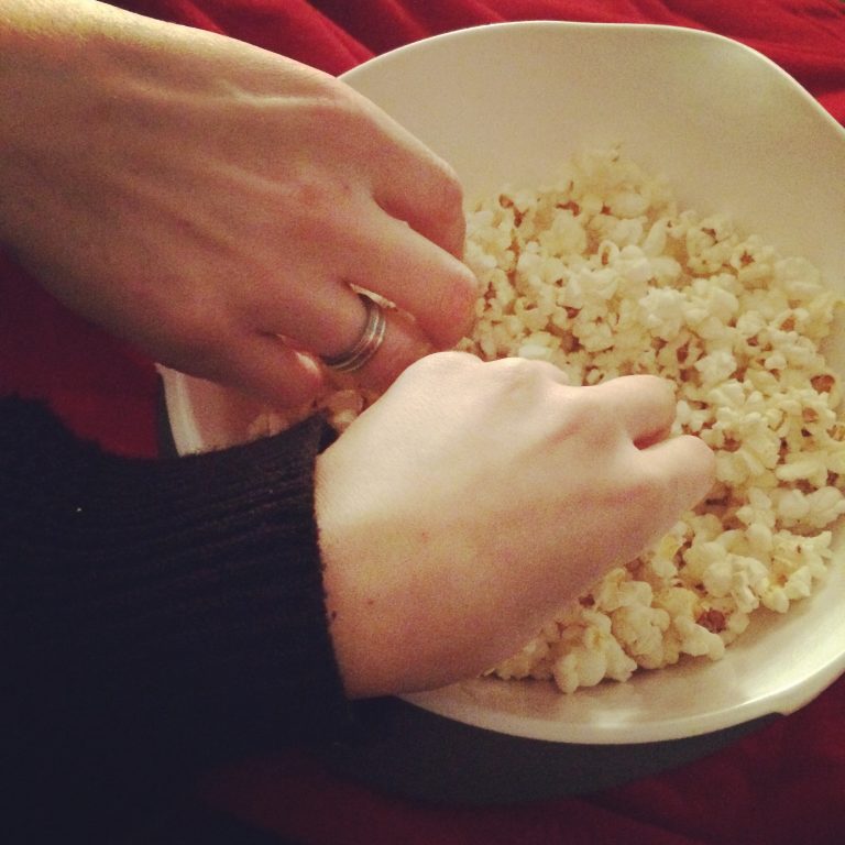 Two hands picking in a popcorn bowl.