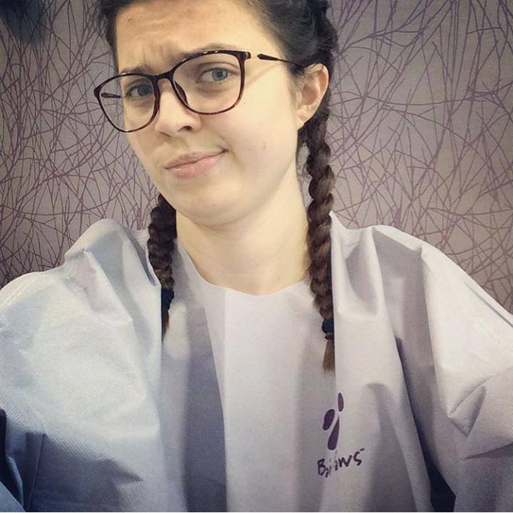 Jenni taking a selfie, wearing a grey gown. Her hair is in plates and she has a confused look.