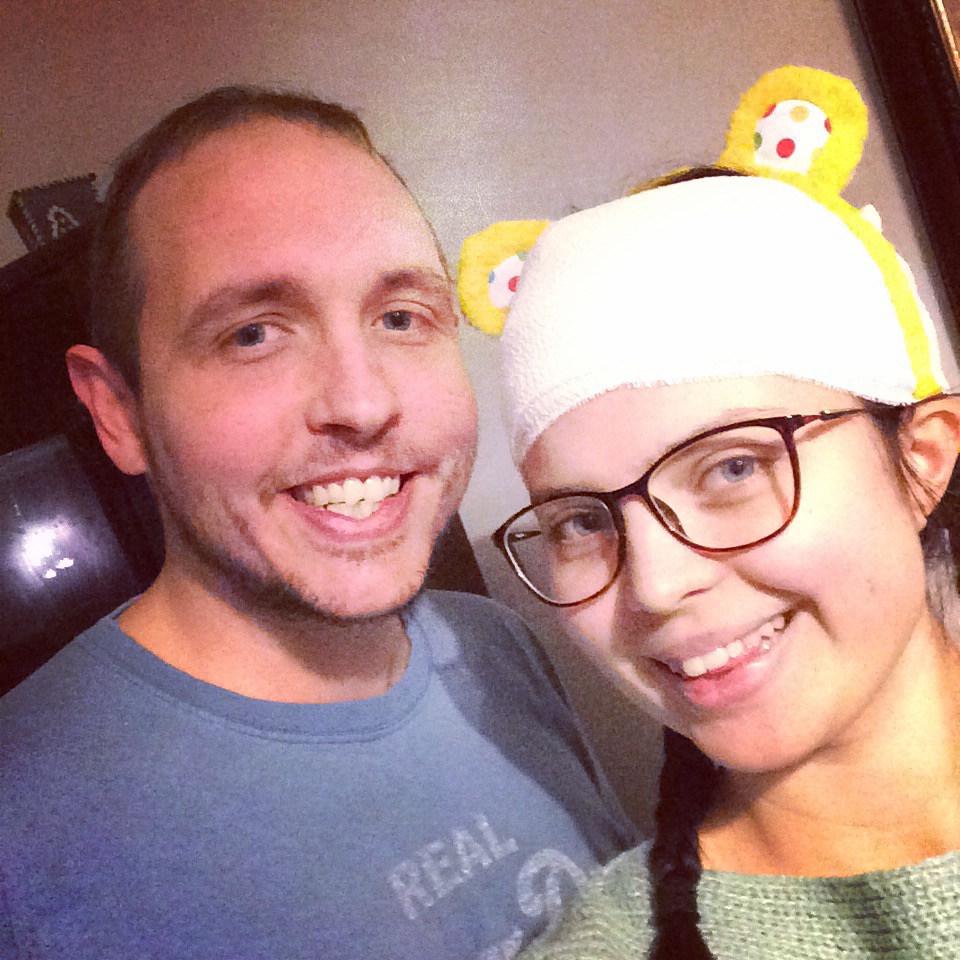 Jenni with a bandage on her head, wearing pudsey bear ears, smiling. Next to her is a gentleman who is also smiling.