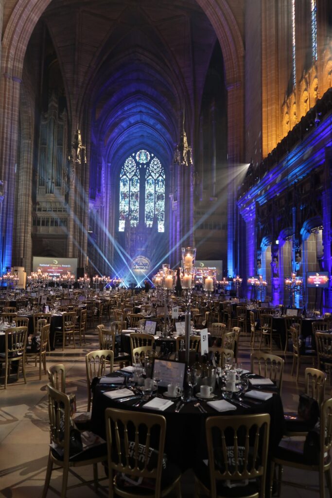 a cathedral with massive stained glass windows with amazing lighting and hundreds of tables with gold chairs and tall candleabras