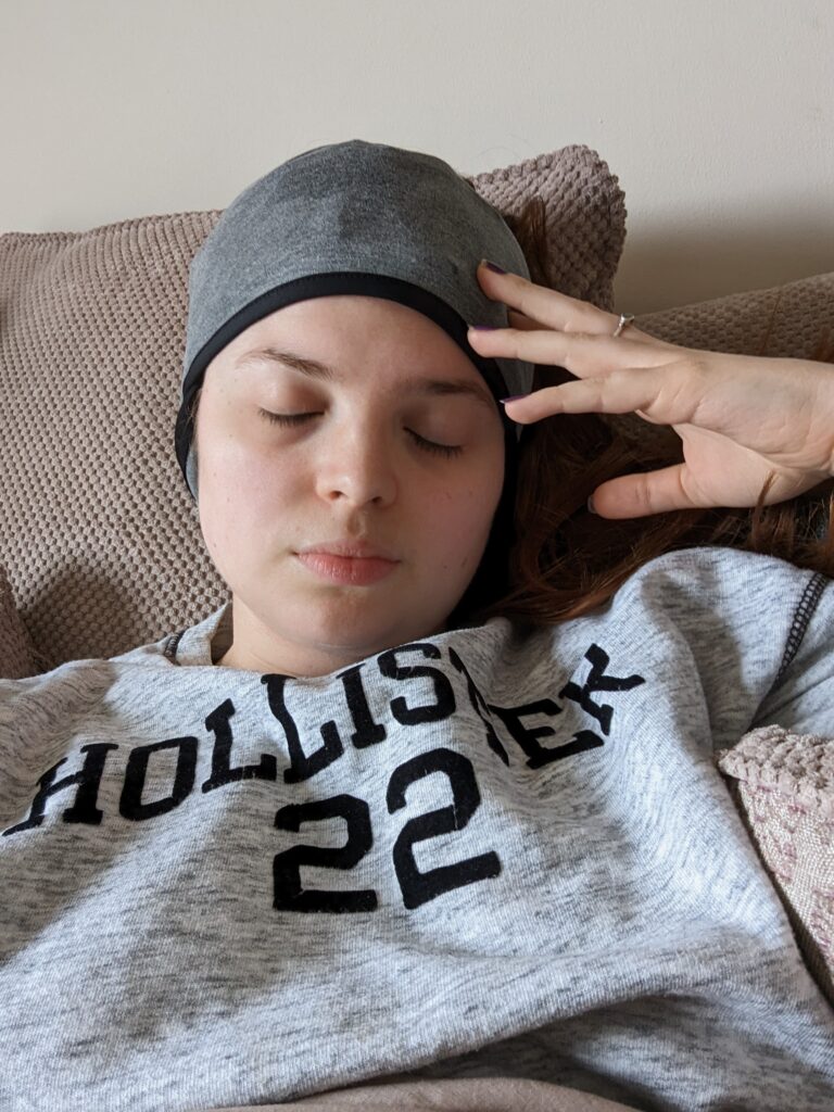 jenni lying on her sofa wearing her headache halo - a grey icepack headband