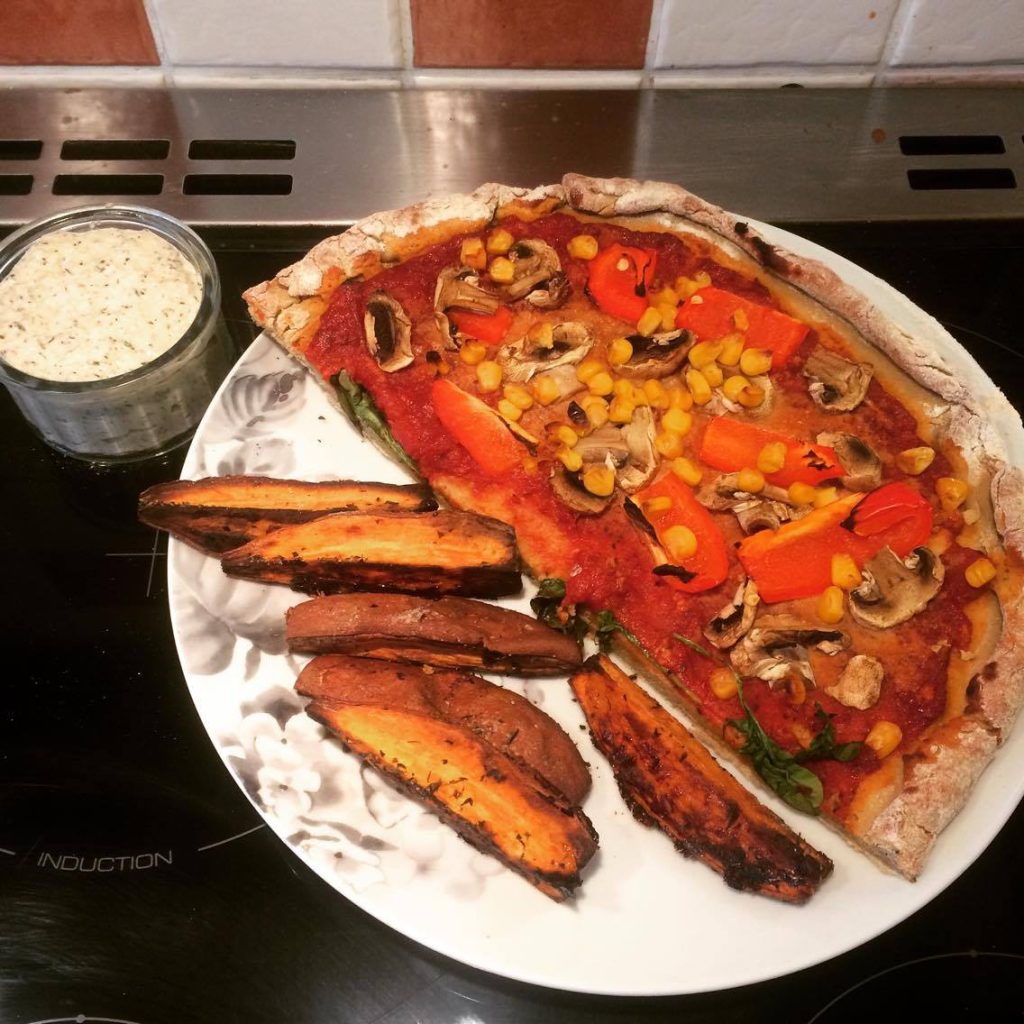 Celebrating Eurovision with A plate with half a pizza which has toppings such as murshrooms and pepper, sitting next to some potato chips and dip.