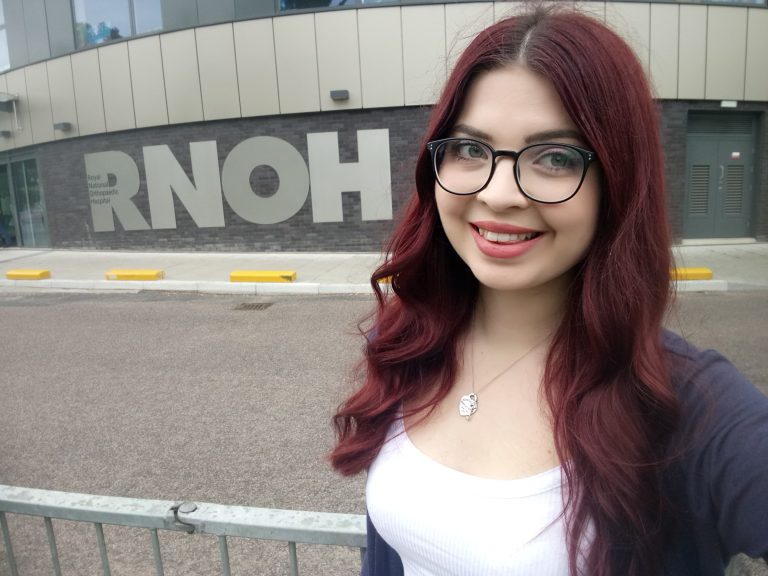 Jenni takes a selfie at RNOH, she is talking about Maintaining Change. She has dark red hair and black glasses.