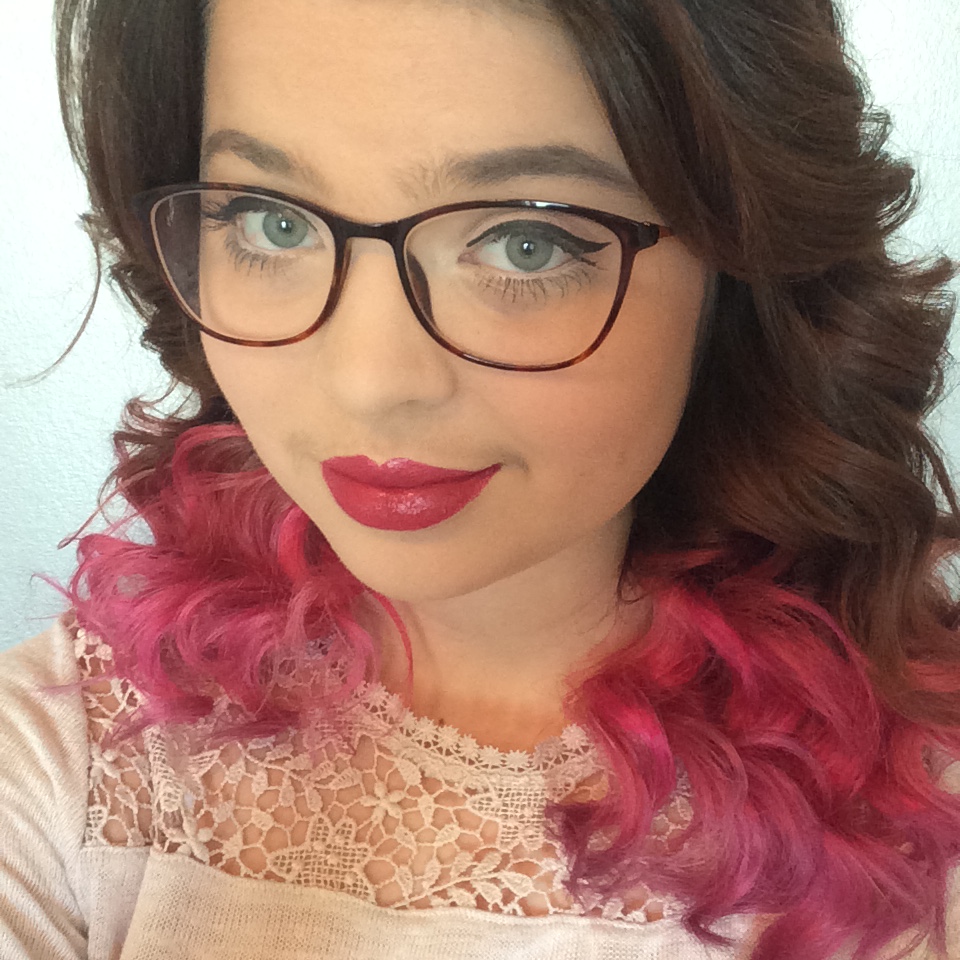A close-up photo of Jennis face, with her brown to pink ombre hair in view. She is wearing a white lace top, and has glasses.