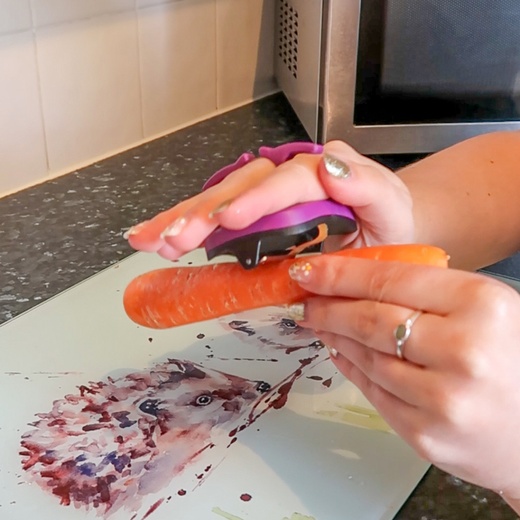 A hand using a Palm Peeler on a carrot