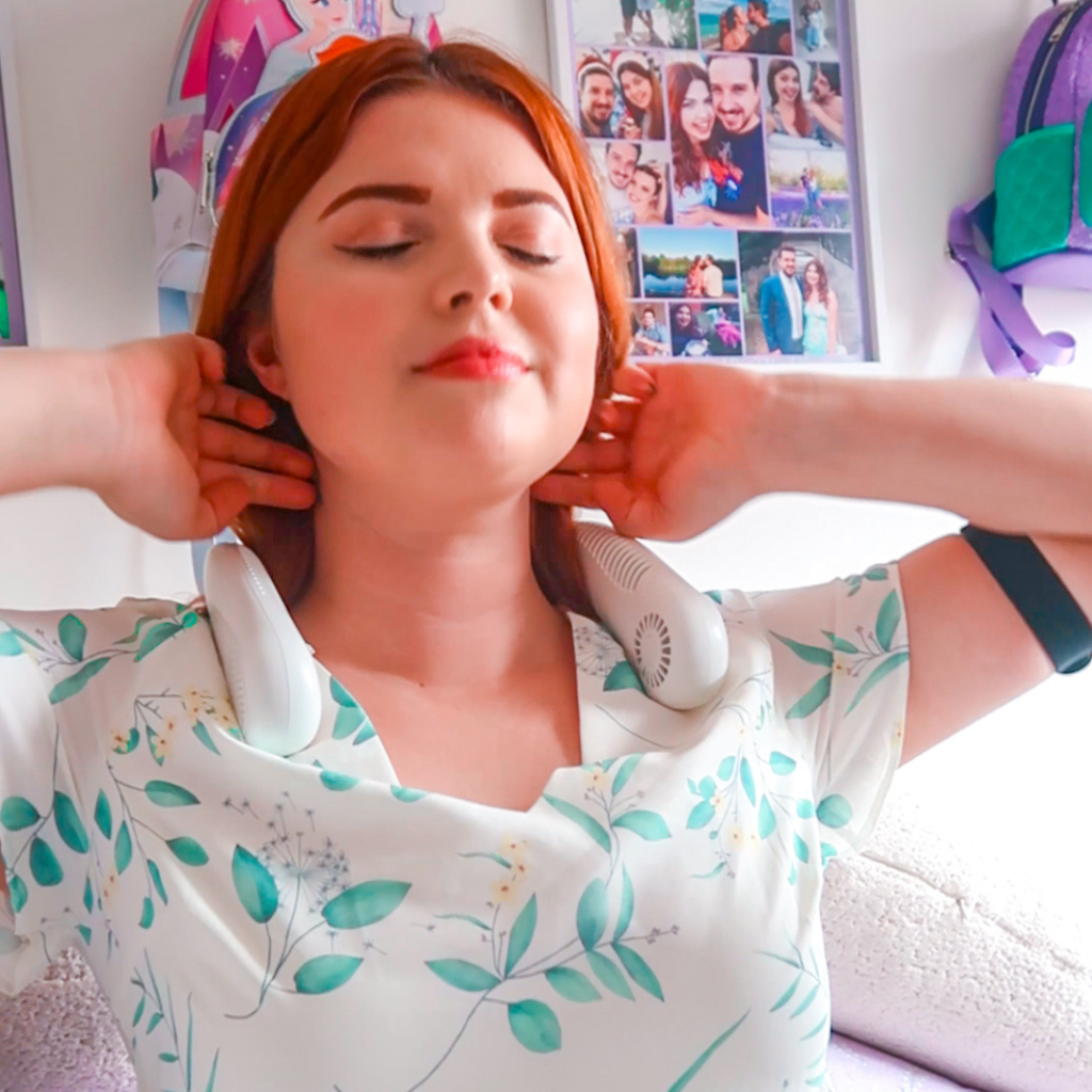 Jenni with her hands behind her head, lifting her hair while wearing a fan.