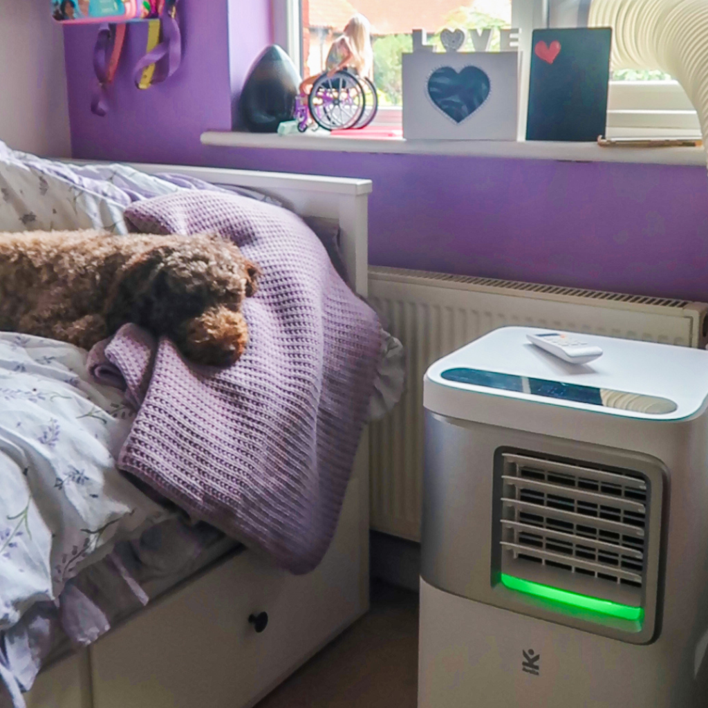 A close up of an air conditioning unit, with Coco the dog asleep on a bed nearby.