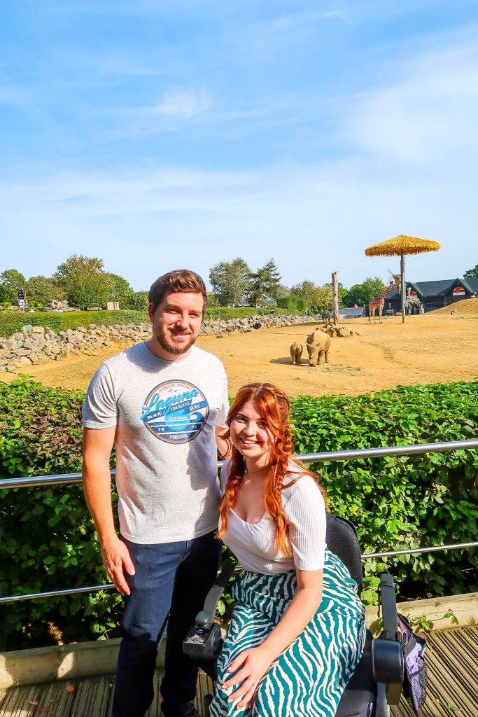 Jenni & her partner Ian at the zoo posing in front of the Rhinos and giraffes