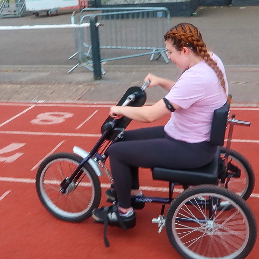 Jenni trying Paralympic Sports using a mobility aid to race at a track.